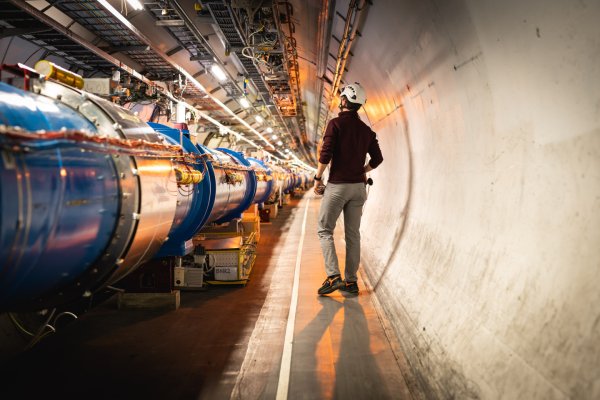 Man met witte helm loopt langs blauwe buizen bij CERN