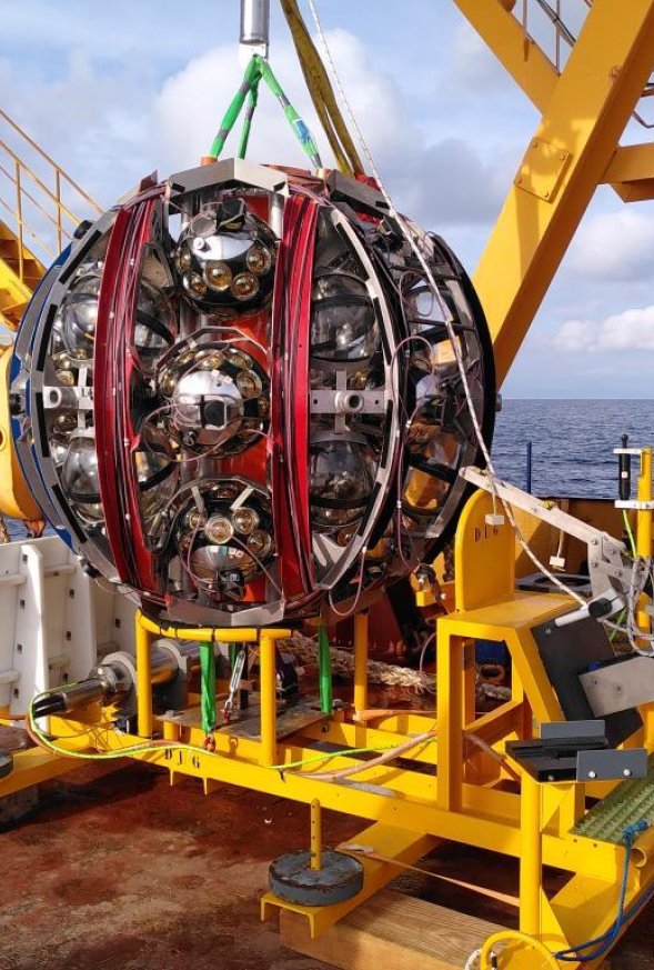 Grote bol van KM3NeT hangt aan een kraan op een schip op zee
