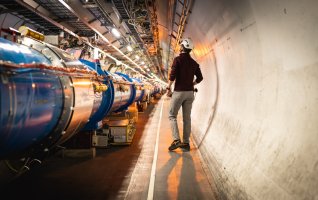 Man met witte helm loopt langs blauwe buizen bij CERN