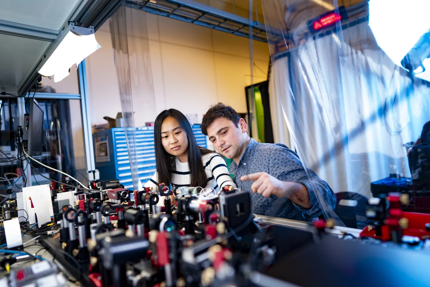 Een vrouwelijke en een mannelijke onderzoeker werken aan een opstelling in een laboratorium op NWO-instituut ARCNL